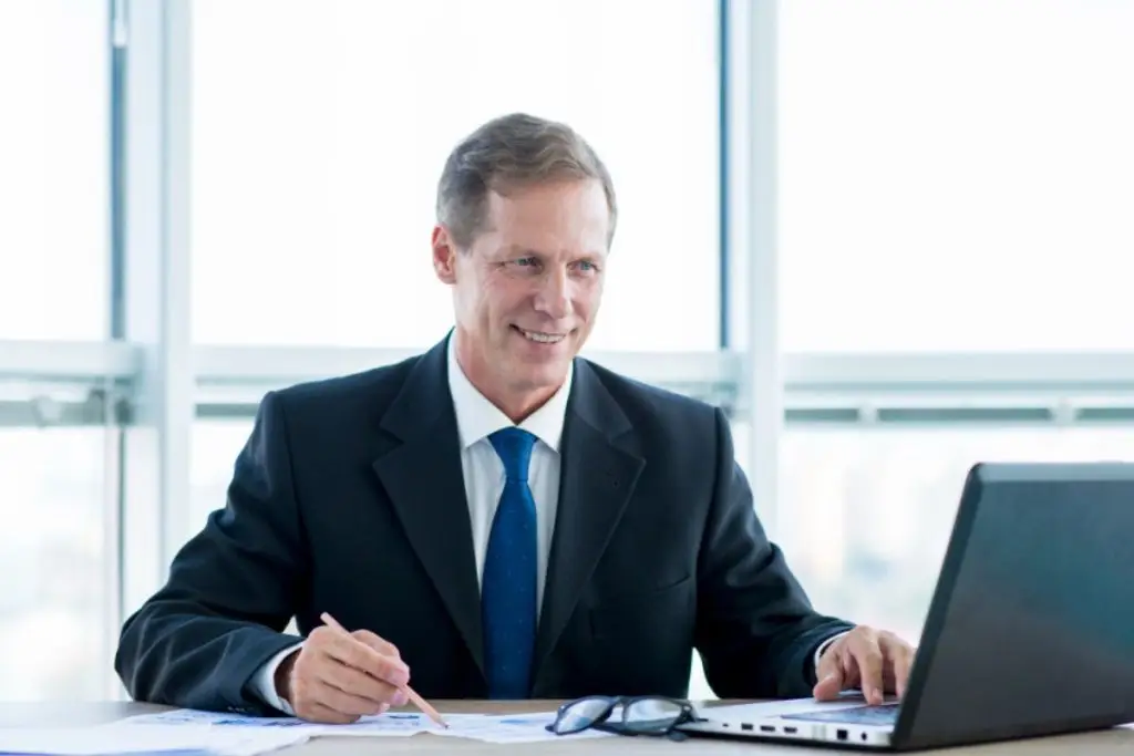 Advogado sorrindo, fazendo anotações e mexendo no notebook, representando um software jurídico gratuito.