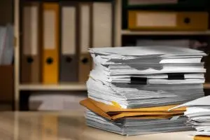 Papéis empilhados sobre uma mesa com uma estante ao fundo, representando a litigância predatória.