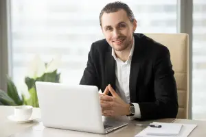 Advogado sorridente com um notebook aberto à sua frente, representando uma gestão de serviços jurídicos.